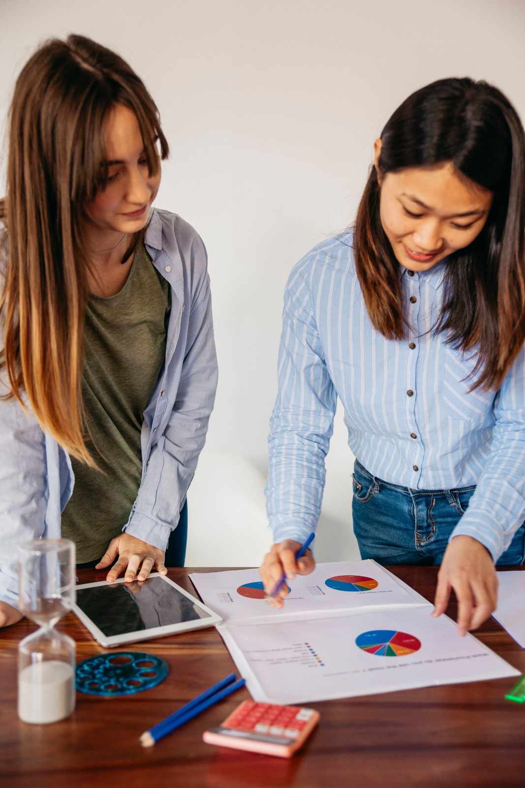 Two female digital marketers reviewing campaign performance pie charts and analytics data.