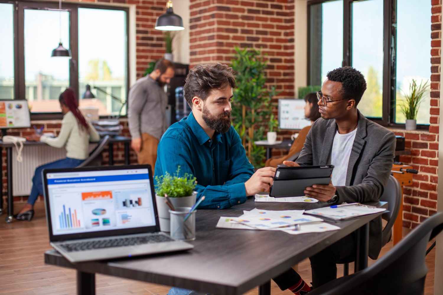 Two marketing professionals reviewing digital campaign performance dashboards on a tablet.