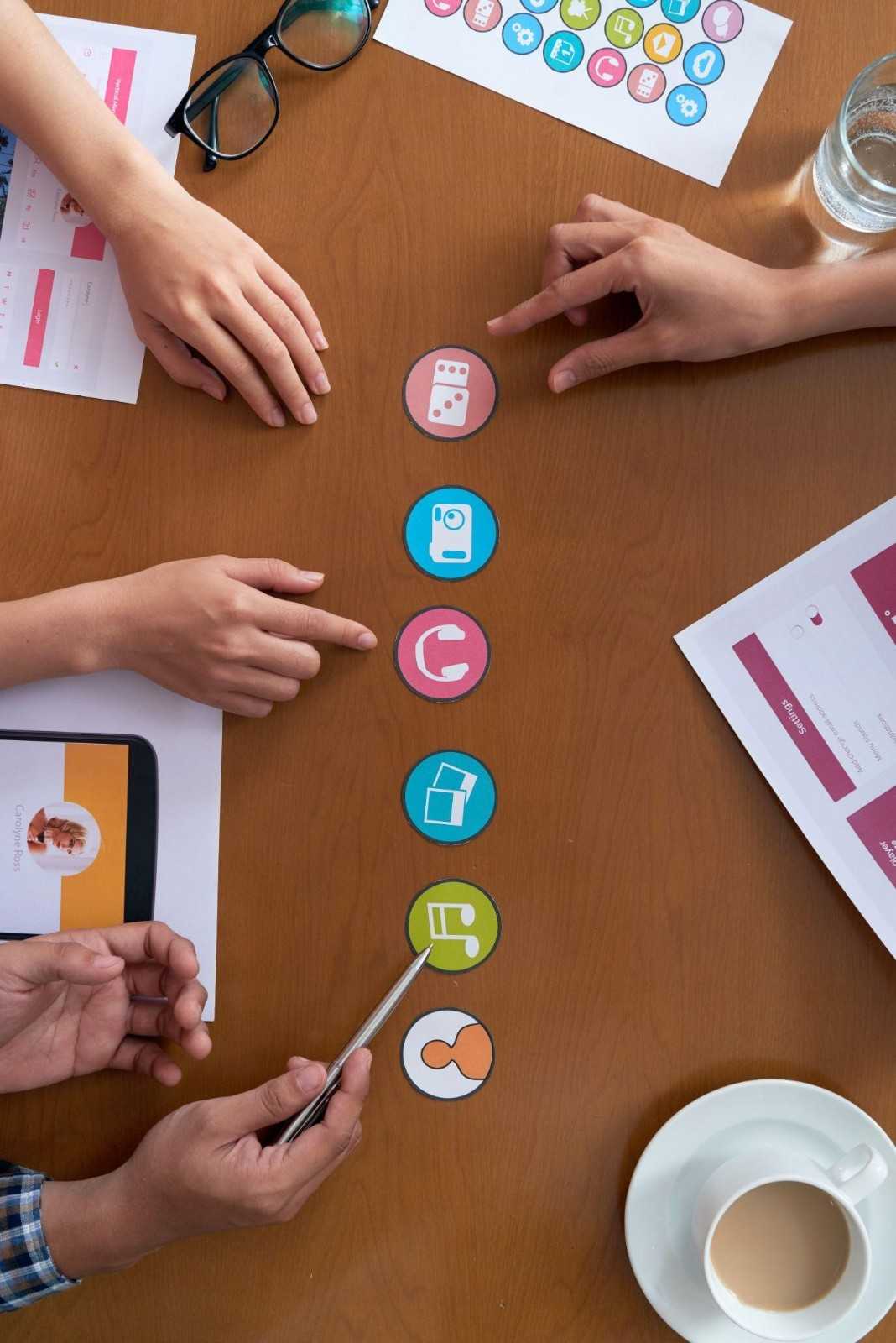 Marketing team pointing at colorful social media icons on a wooden desk.