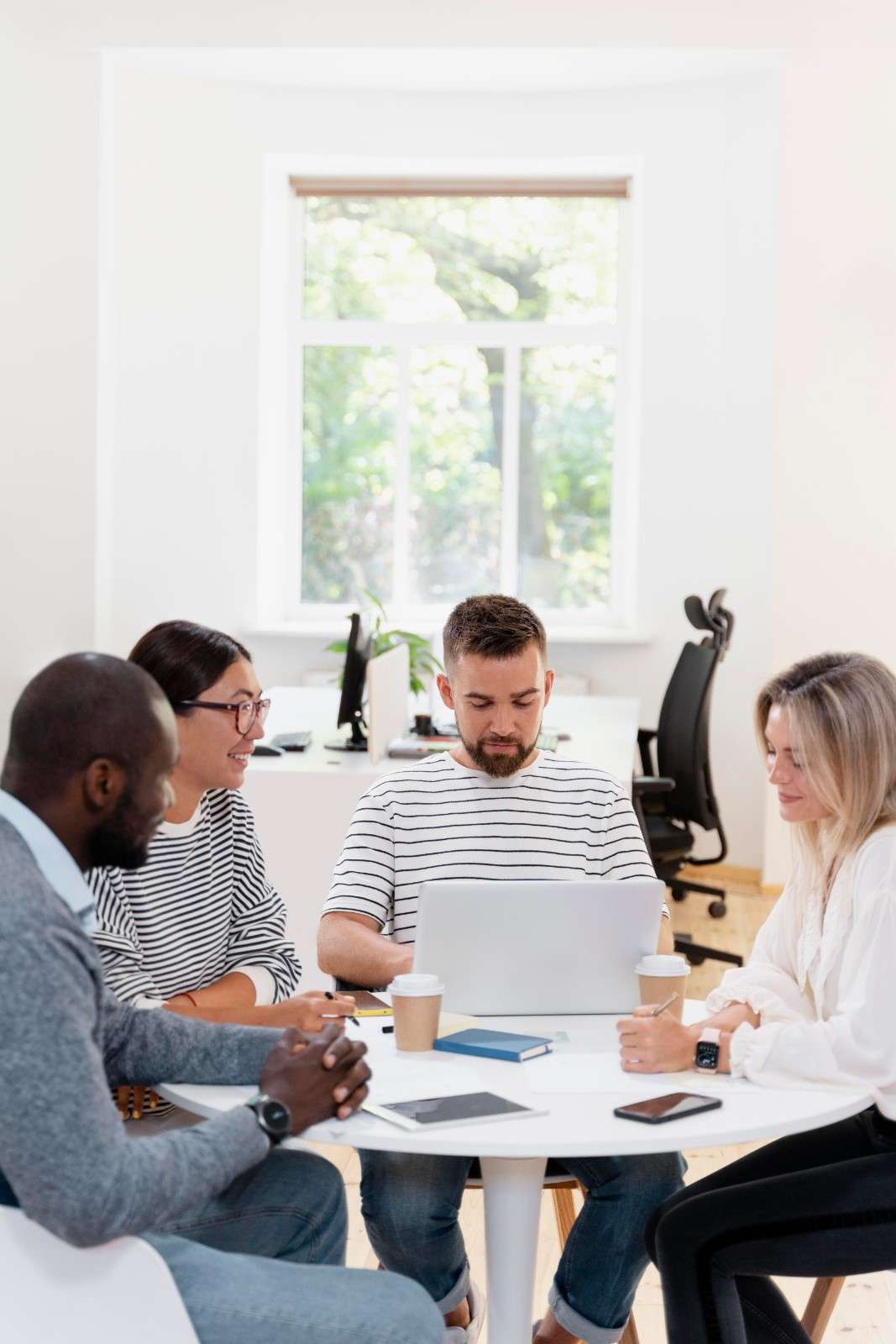 Four digital marketing colleagues collaborating around a laptop during an office strategy meeting.