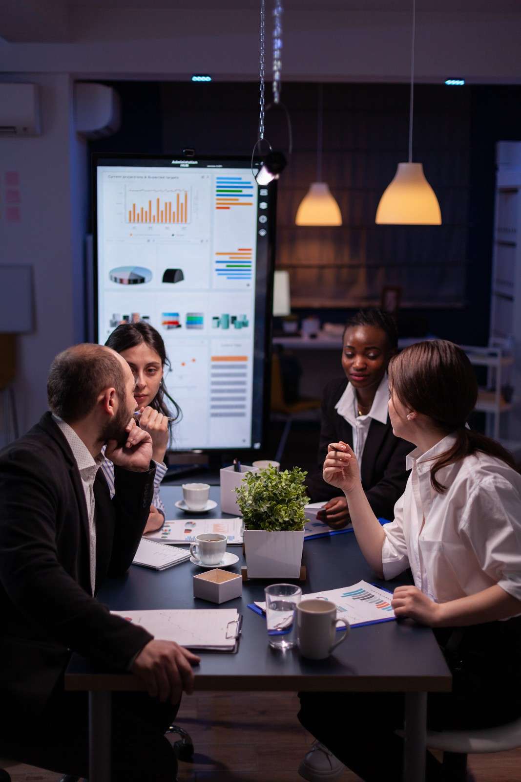 Business team analyzing financial charts and data on a large screen during a late-night office meeting.