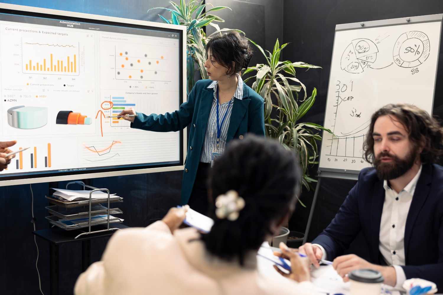 A team leader pointing to analytics on a smart board while discussing strategy with colleagues in an office.