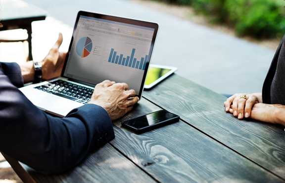 Professional presenting financial charts and expense reports on a laptop screen during a business consultation at an outdoor meeting table.
