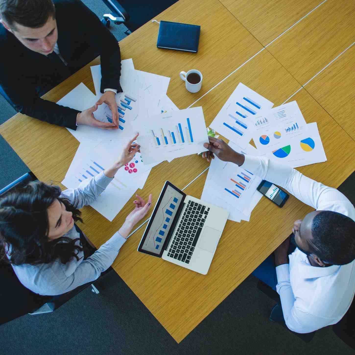 Overhead view of a business team analyzing data charts and a laptop on a wooden table.