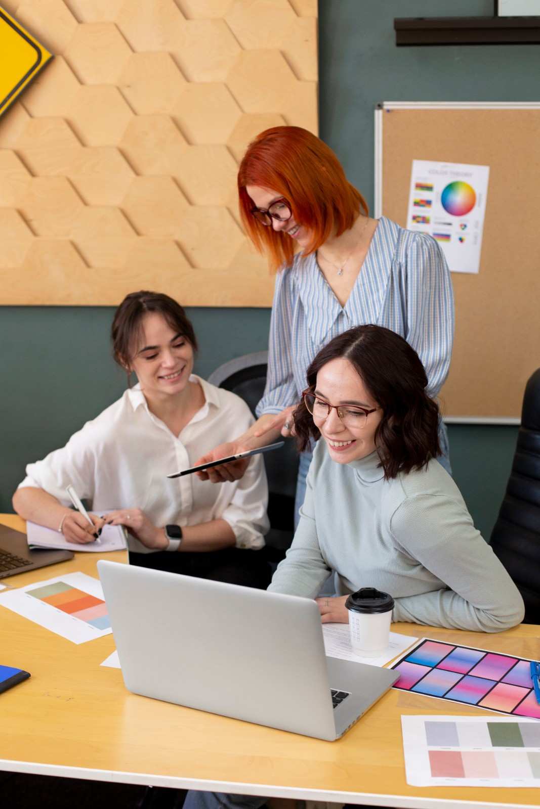 A creative team of three women smiling and collaborating on a marketing project using a laptop and tablet.